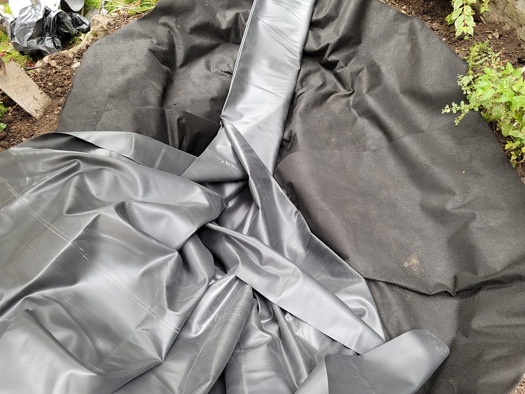 Underlay in position and liner being laid during the pond construction process